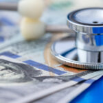 Closeup of a stethoscope on top of hundred dollar bills, illustrating the blog topic The Future of Health Insurance and Plan Options with the Trump Administration