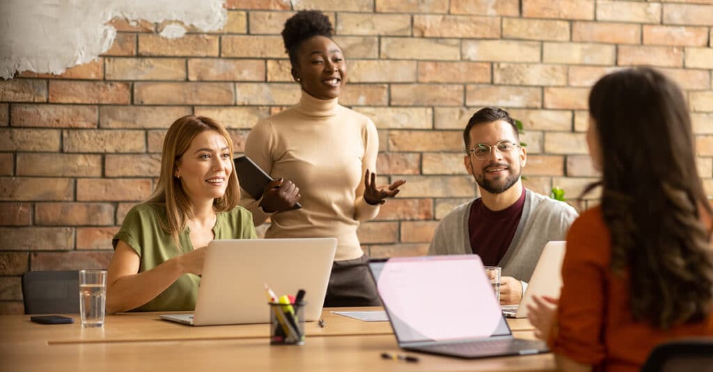 Young, diverse group of professionals working at a conference table with a brick background, illustrating the blog topic of Big Benefits for Small Teams: Health Insurance Options that Work