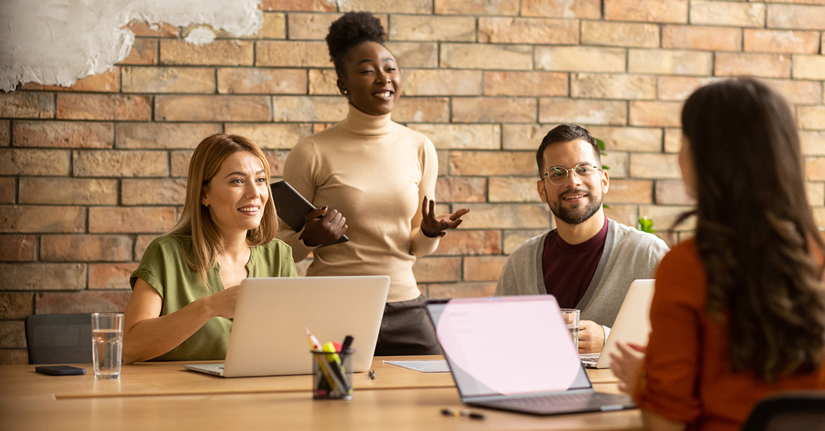 Young, diverse group of professionals working at a conference table with a brick background, illustrating the blog topic of Big Benefits for Small Teams: Health Insurance Options that Work