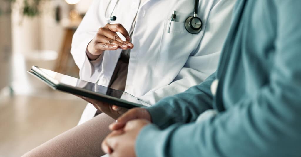 Close-up and cropped image of a physician and patient sitting together discussing something on a tablet, illustrating the blog topic "What is Direct Primary Care?"