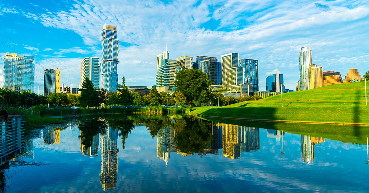 Beautiful sunny afternoon cityscape skyline of Austin, Texas, with buildings and lush green landscape reflecting dramatically in the water in the foreground