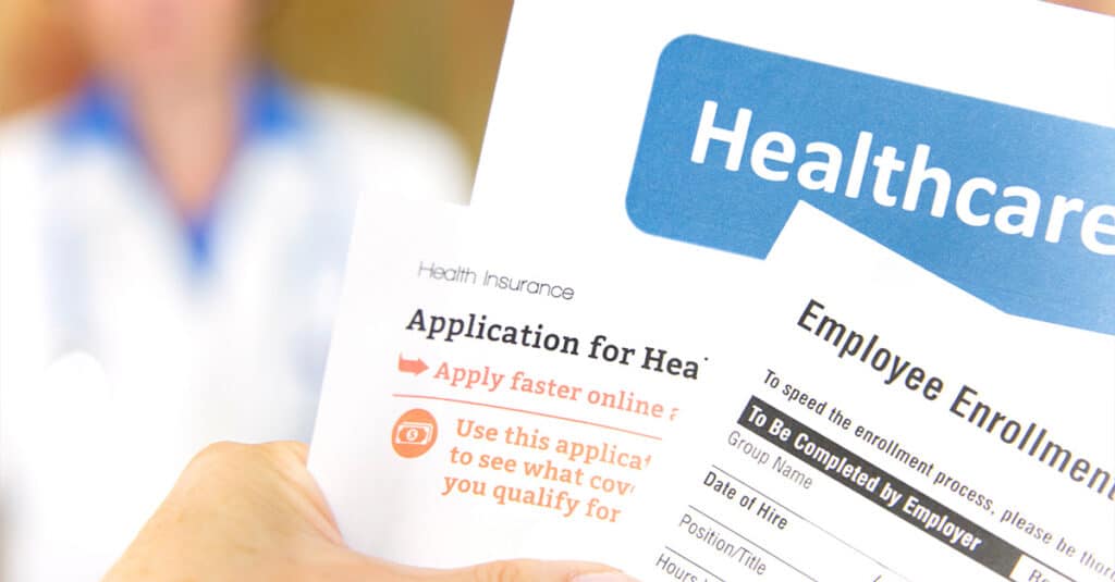 Open enrollment healthcare benefits forms with a medical doctor in the background.